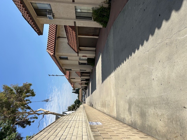 A view of a street with a building on the left and a wall on the right.