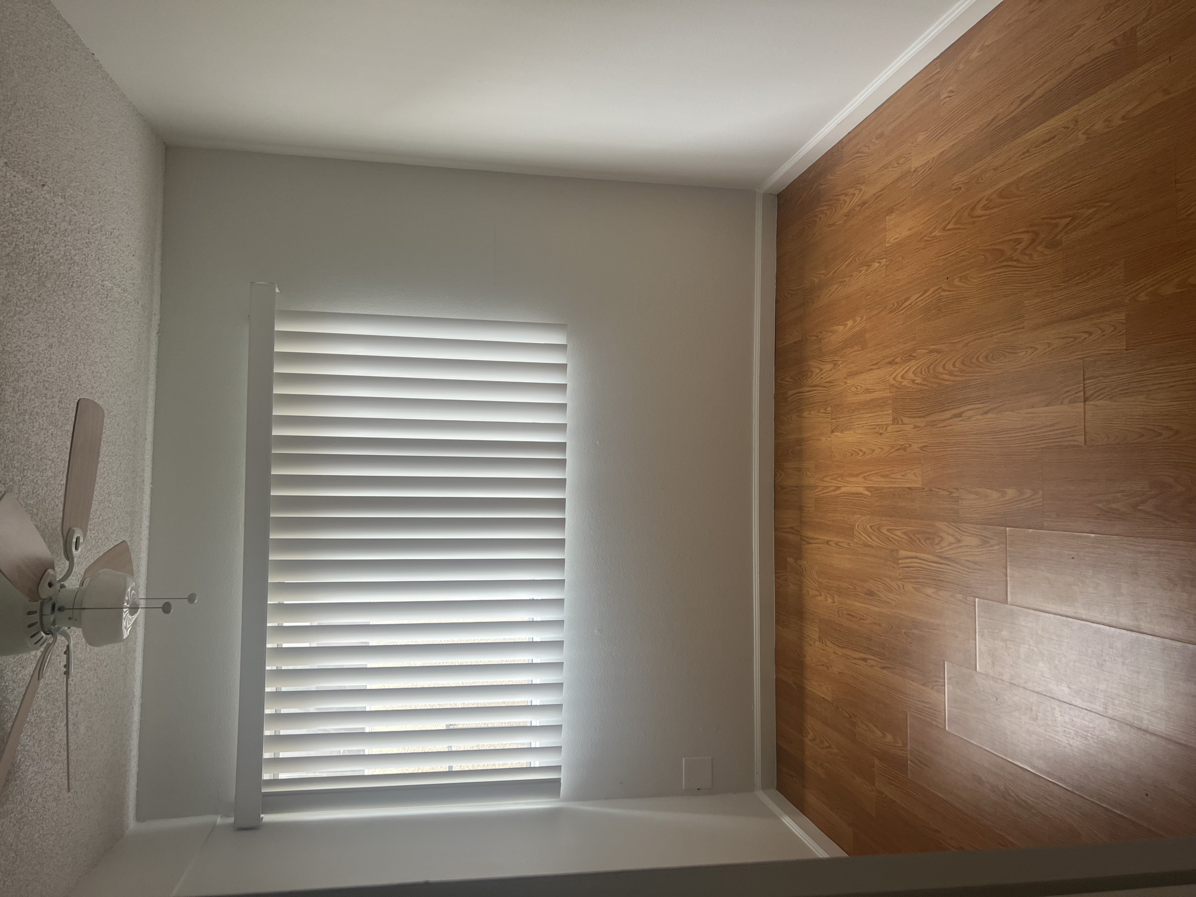 A room with a ceiling fan and wooden wall paneling.