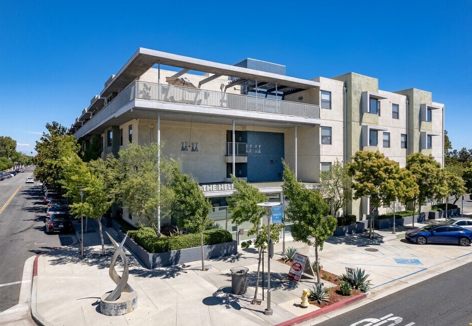 an apartment building with a parking lot and trees in front of it at Helix at University Village, Pomona, CA