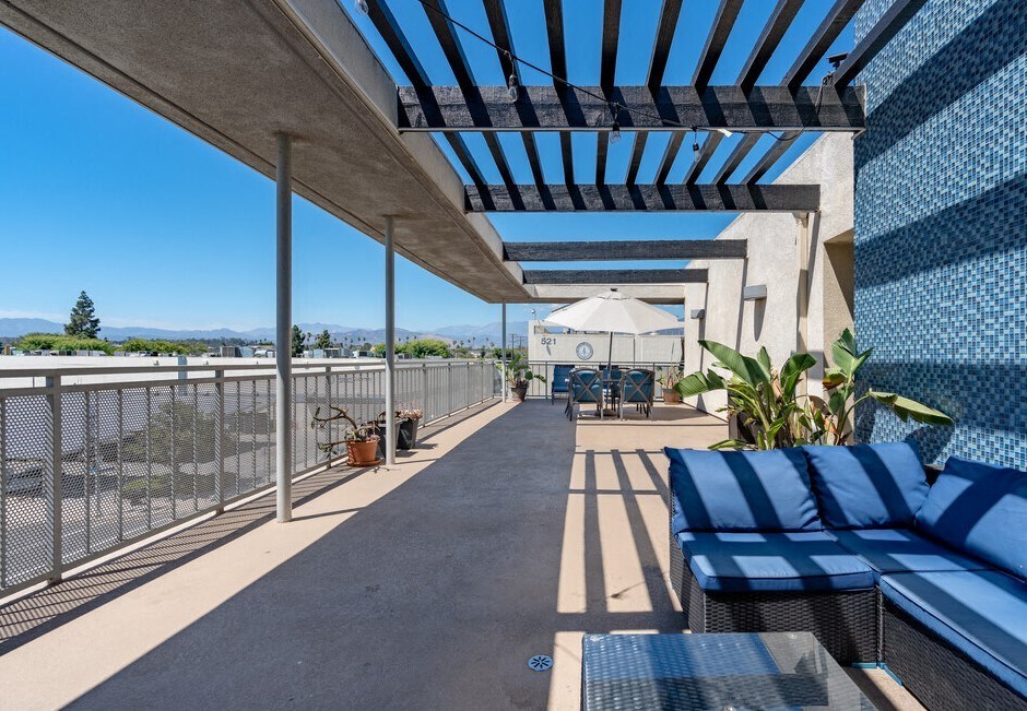 a patio with blue lounge chairs and a white umbrella on a sunny day at Helix at University Village, Pomona, CA 91766