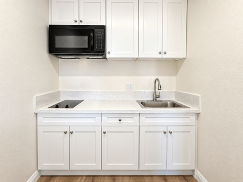 A kitchen with white cabinets and a black microwave.