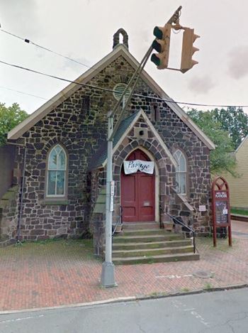 A small stone building with a red door and a sign on the right.