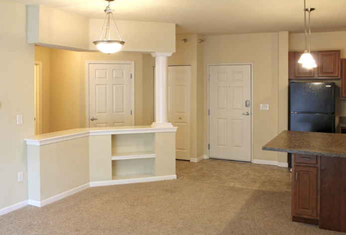 an empty living room with a kitchen in the background