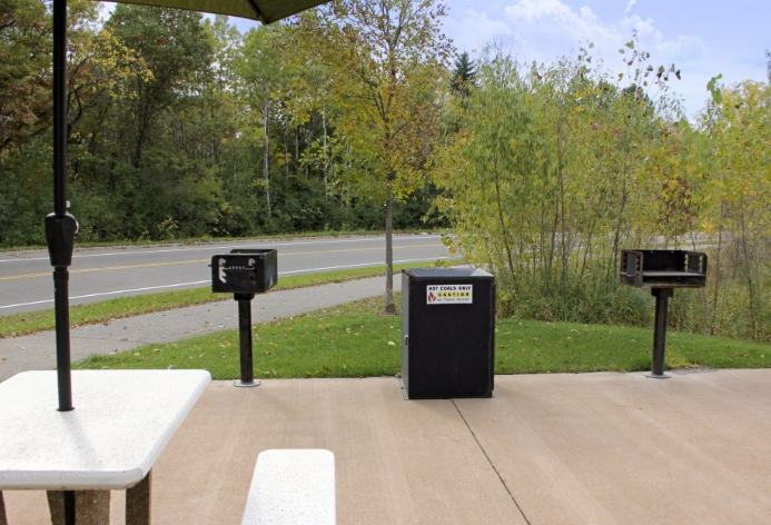 a picnic table with trash can and a road in the background