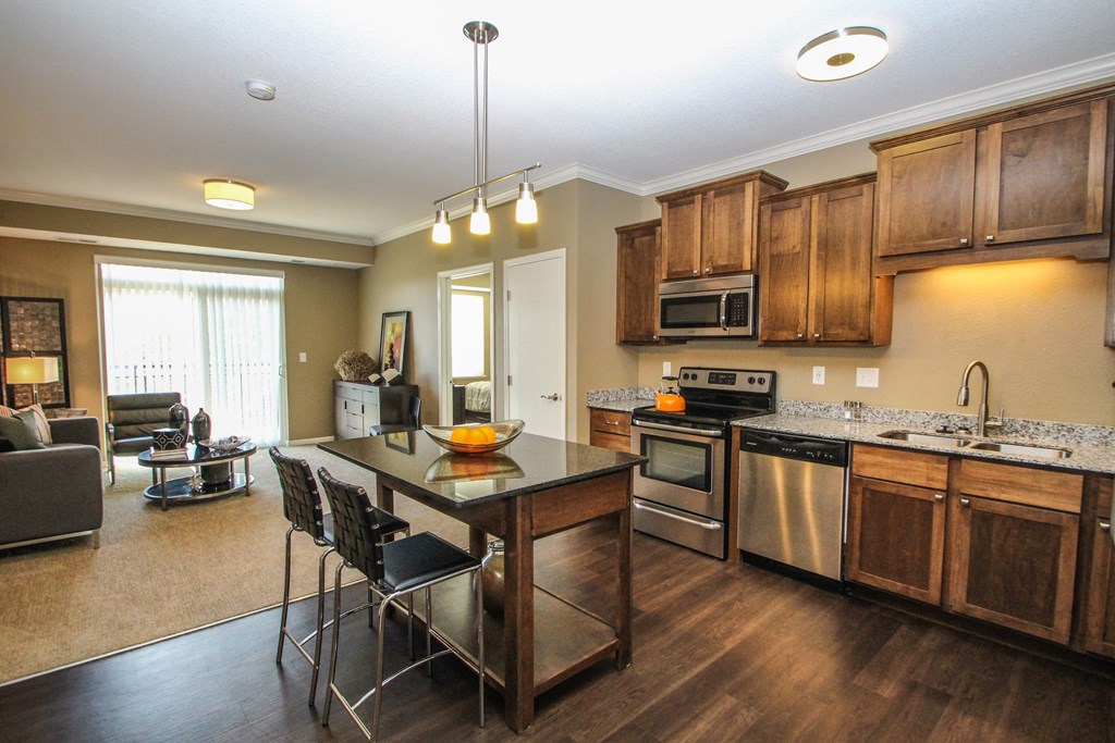 a kitchen with a center island and a living room in the background at The Flats at Cedar Grove, Eagan