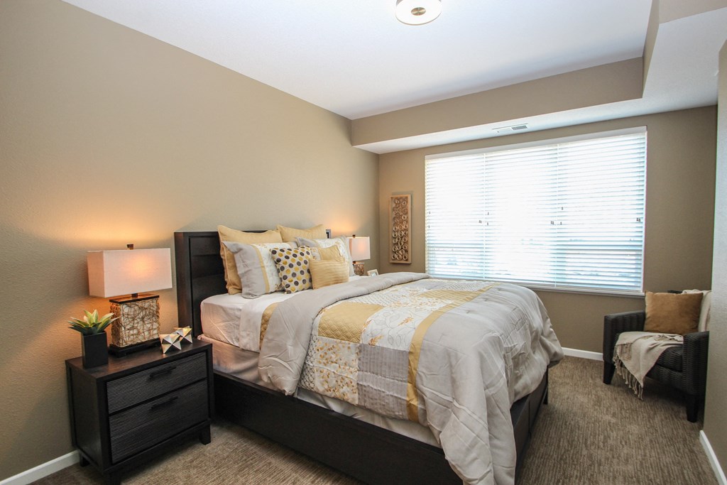 a bedroom with a bed and nightstand with a lamp on top of it at The Flats at Cedar Grove, Eagan, MN, 55122
