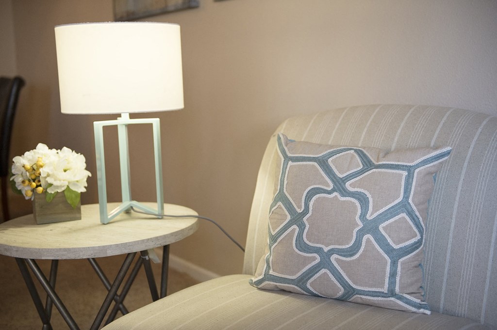 a chair with a pillow on it next to a table with a lamp and a vase at Hearthstone Apartments and Townhomes, Apple Valley, 55124