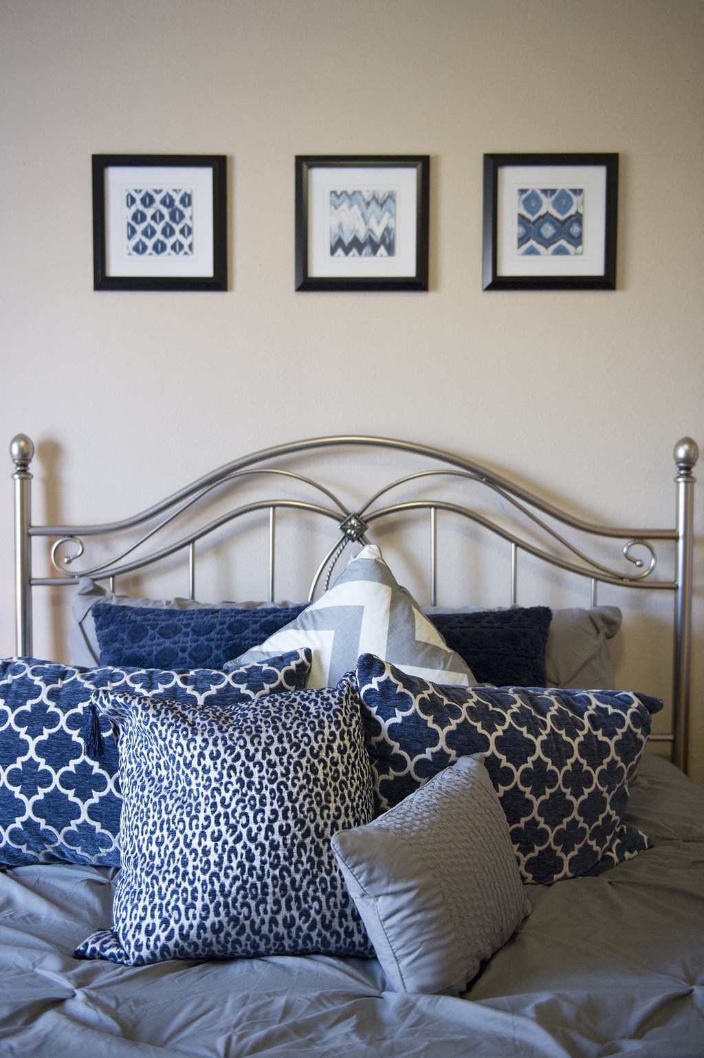 a bedroom with a bed with blue and white pillows and three framed pictures on the wall at Hearthstone Apartments and Townhomes, Apple Valley, MN