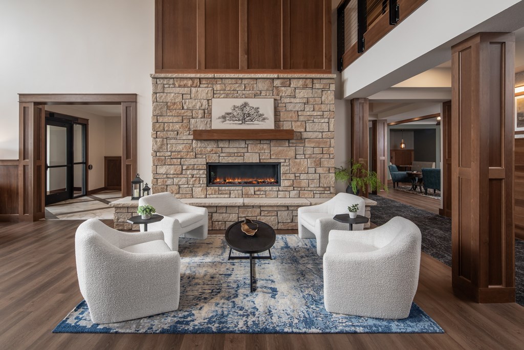 A living room with a stone fireplace and white chairs.