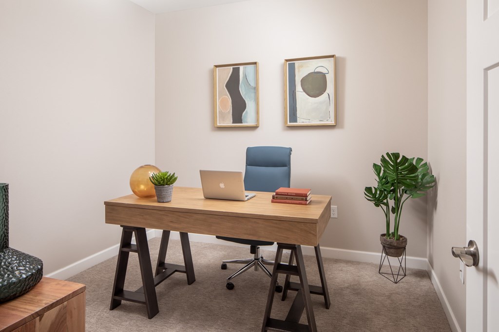 A room with a desk, chair, and two framed artworks on the wall.