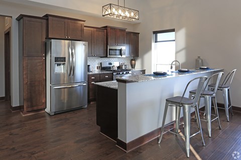 A kitchen with a refrigerator, stove, and bar stools.