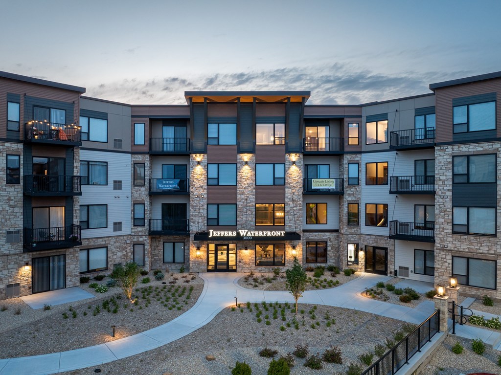 The image shows a modern multi-story residential building named "Jeffers Waterfront" with a well-lit entrance and balconies on the upper floors.