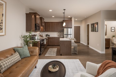 A brown leather couch with a green pillow is in the foreground of a modern kitchen and living room.