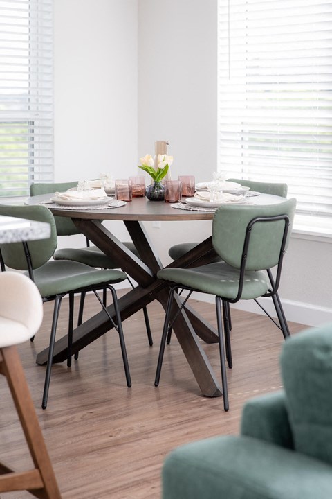 Dining area with round wood table and sage green chairs at The Carver Apartments, Chaska, MN 55318