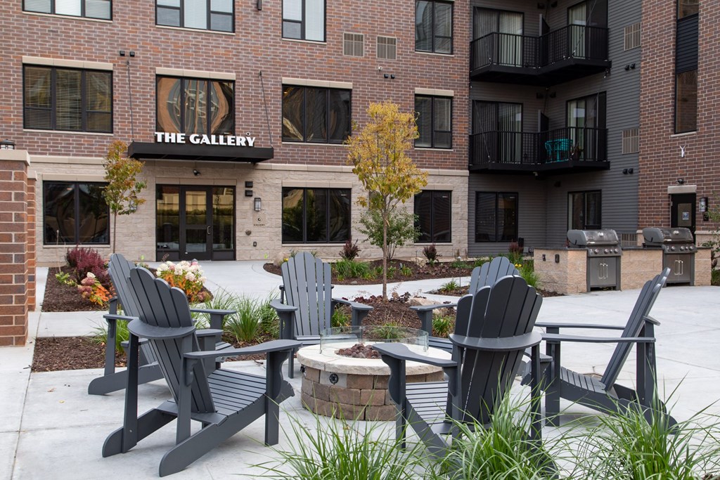 a patio with three adirondack chairs and a fire pit in the center at The Gallery Apartments, Burnsville, 55337