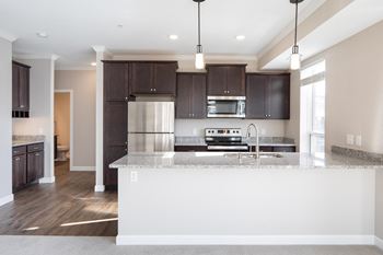 a kitchen with dark wood cabinets and a large island with granite countertopsat The Carver Apartments, Chaska, MN 55318