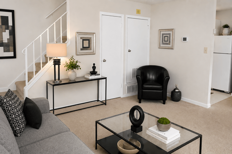 A black chair sits in a living room with a grey couch and a glass coffee table.