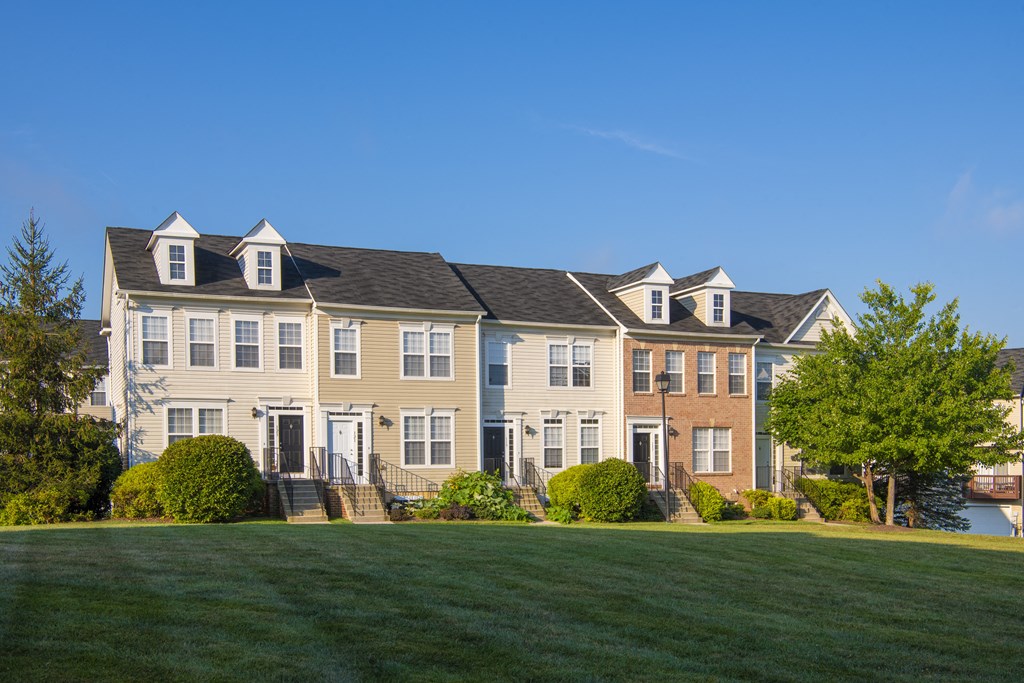 a row of houses on a green lawn with a blue sky at Townes at Village Center Apartments, Reisterstown, 21136