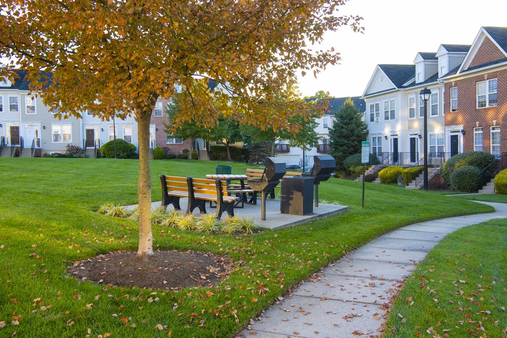 a park with a bench and a tree in front of houses at Townes at Village Center Apartments, Reisterstown, Maryland