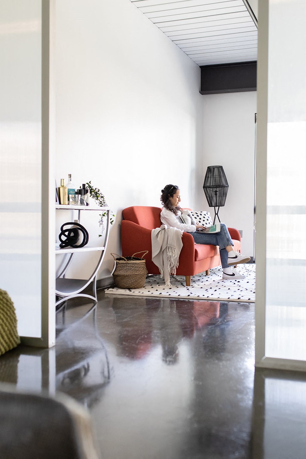a woman sits in a red chair in a white room with a black lamp and a white