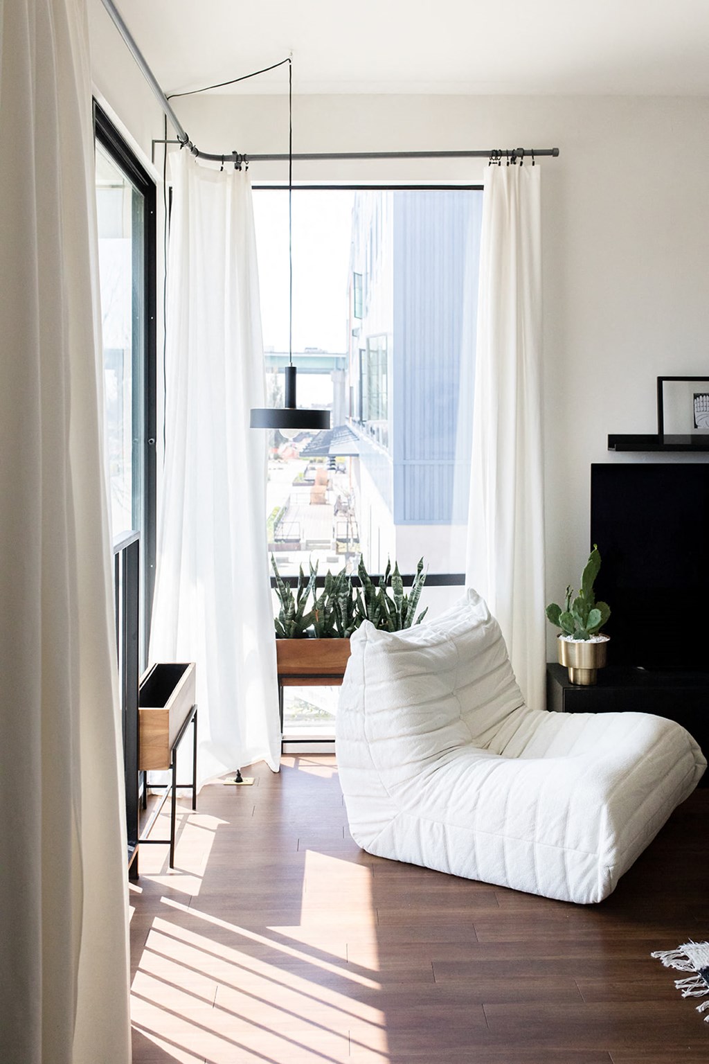 a living room with a white chaise lounge and windows with white curtains