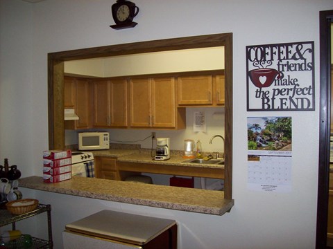 A kitchen with a mirror, a microwave, a coffee maker, and a calendar on the wall.