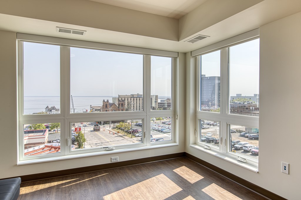 A room with a view of a parking lot and buildings outside the window.