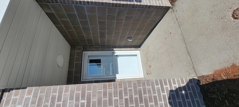 A small window on a house with a brown brick wall.