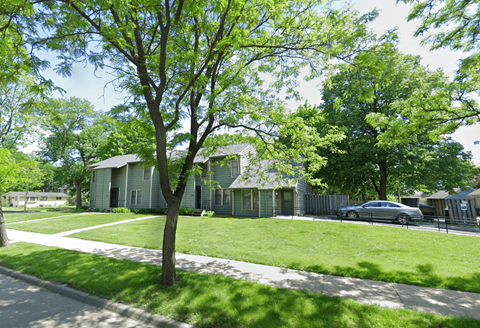 A tree in front of a house with a car parked in the driveway.