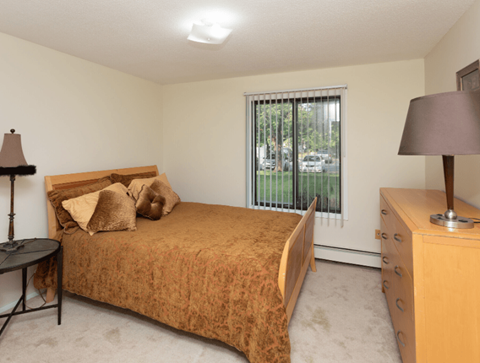 A bedroom with a bed, nightstand, and window with blinds.