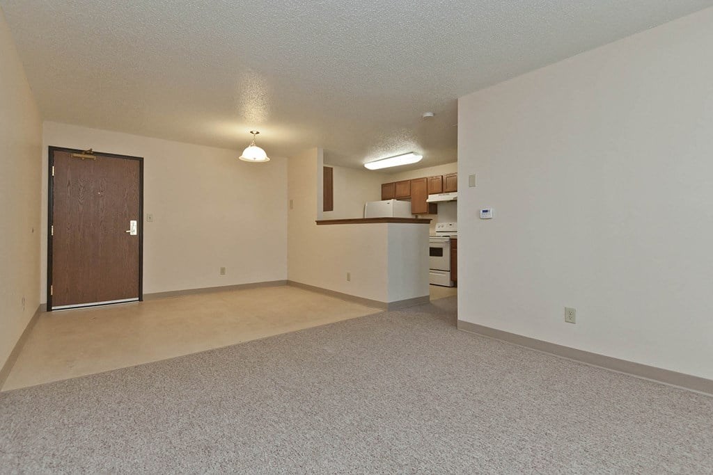 A spacious room with a door and a kitchenette in the background.