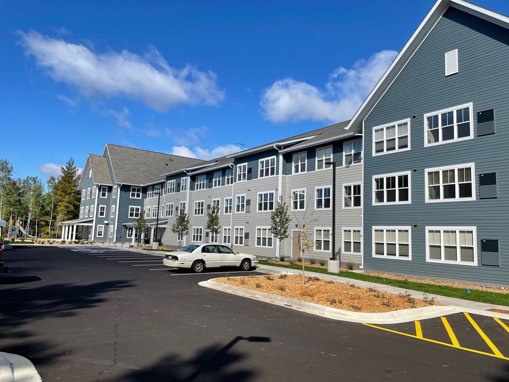 A white car is parked in a parking lot in front of a grey building.