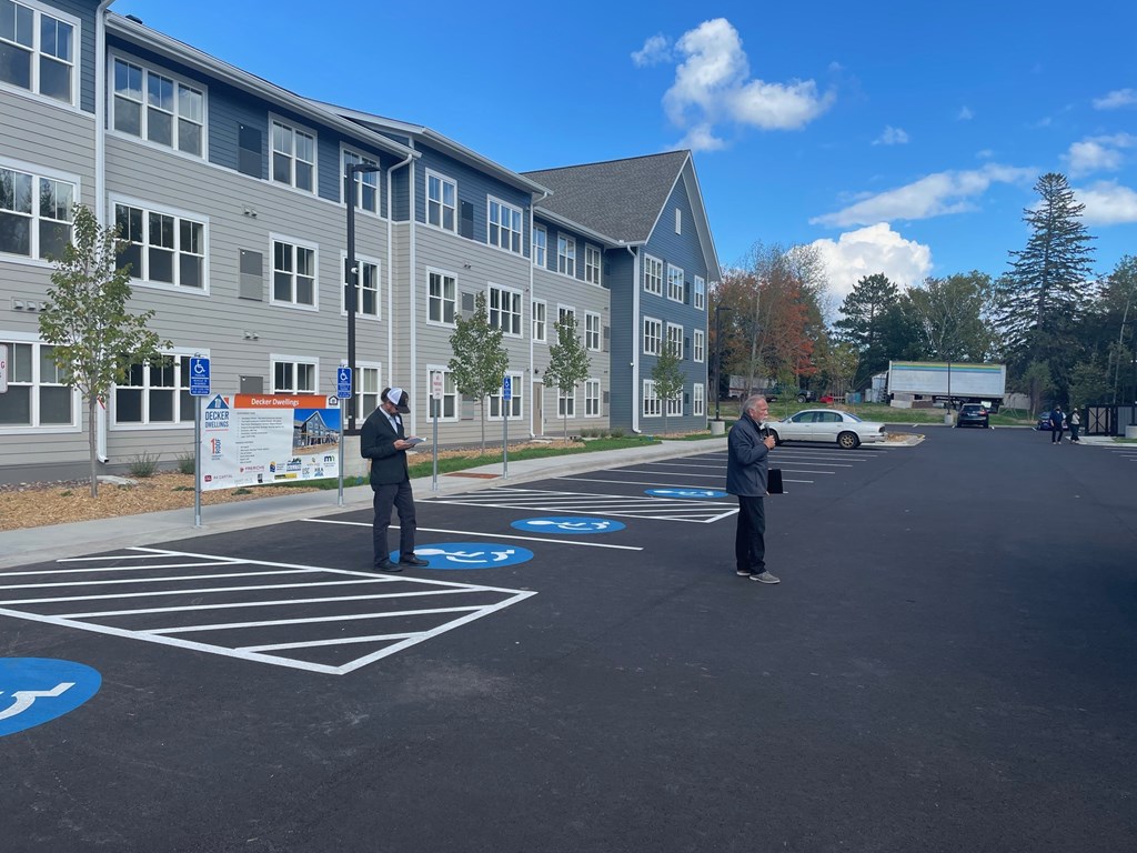 Two men standing in a parking lot with a building in the background.