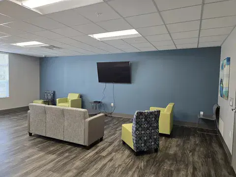 A room with a couch, chairs, and a television.