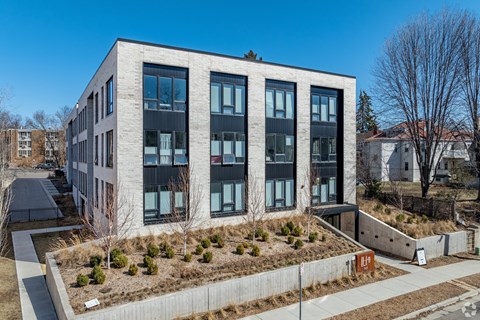 A modern building with a grey and black facade and a small garden in front.