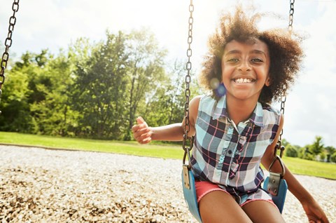 A girl is sitting on a swing in a park.