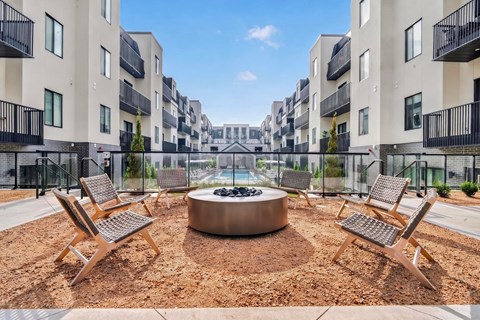 A modern courtyard with a fire pit surrounded by chairs and buildings.
