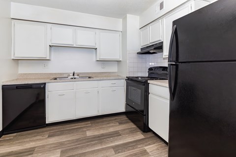 A black refrigerator is on the right in a kitchen with white cabinets.