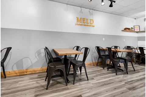 A dining area with chairs and tables in front of a wall with the word MELD on it.
