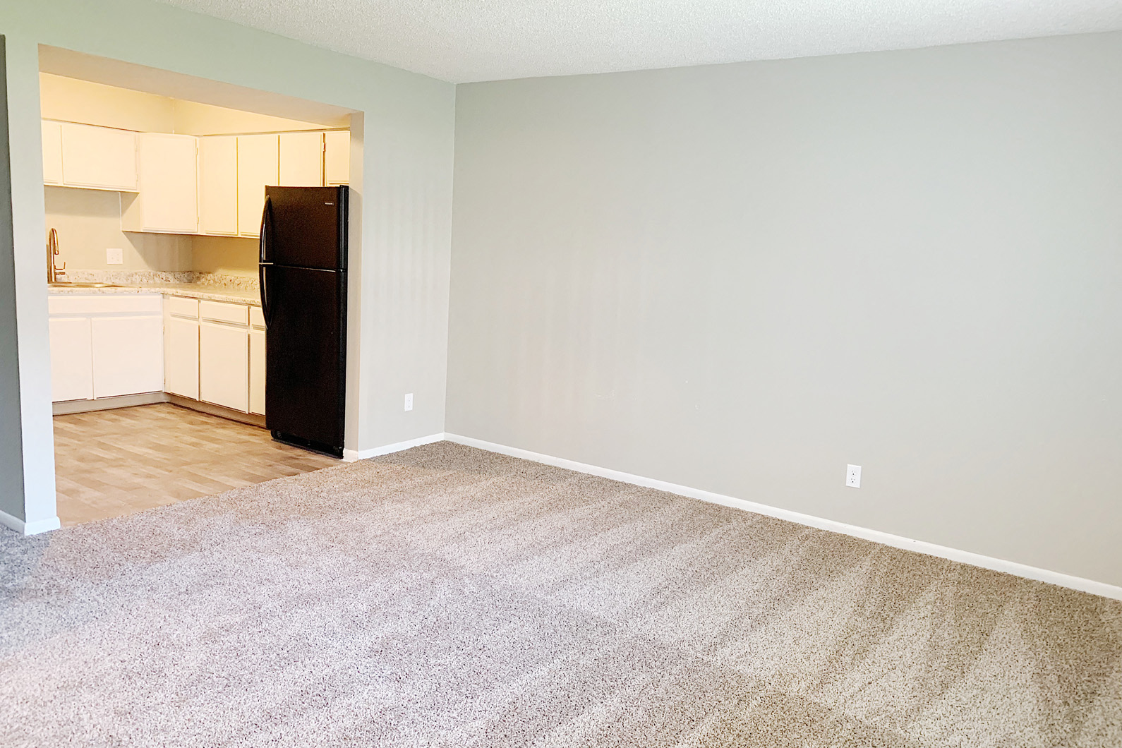 an empty living room and kitchen with a refrigerator