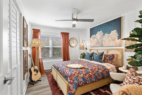 A bedroom with a bed, a guitar, a clock, a plant, and a painting on the wall.