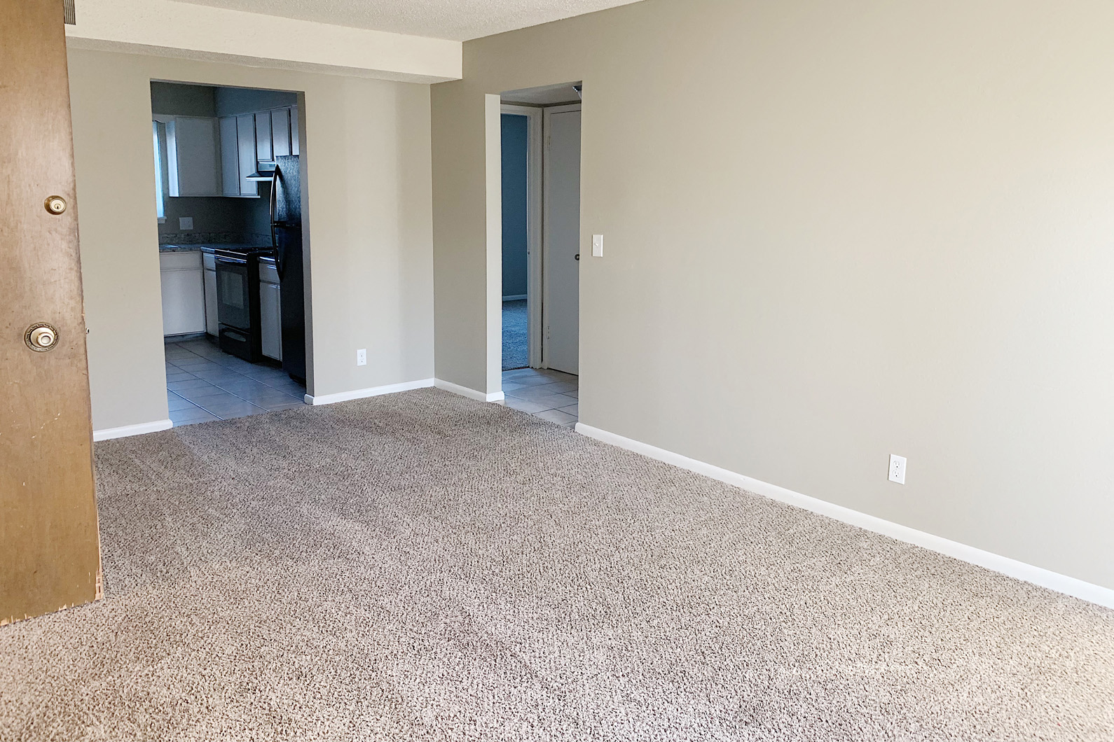 an empty living room with carpet and a kitchen