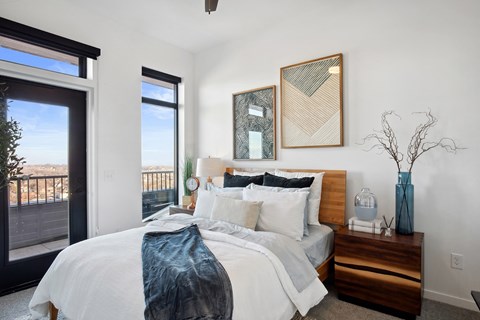 A bedroom with a large bed and a balcony overlooking the city.