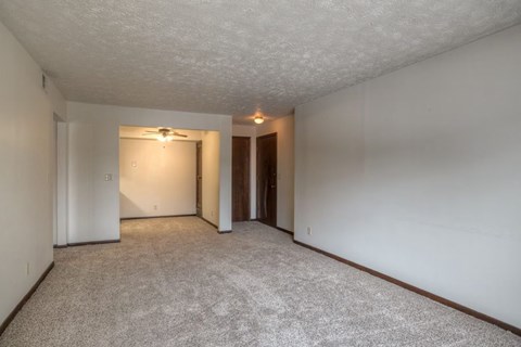 A sparsely furnished room with a carpeted floor and a ceiling fan.