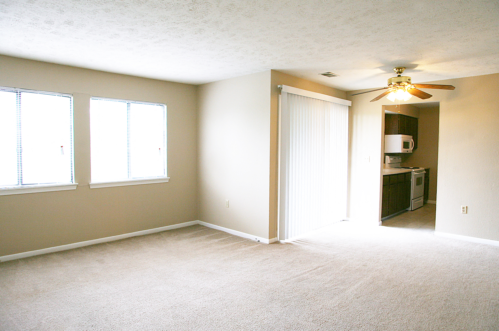 an empty living room with a ceiling fan and a kitchen