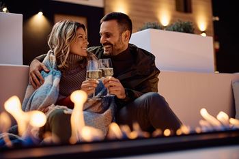 A couple is sitting on a bench with a glass of wine, surrounded by lit candles.