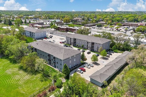 A large grey building surrounded by a parking lot and greenery.
