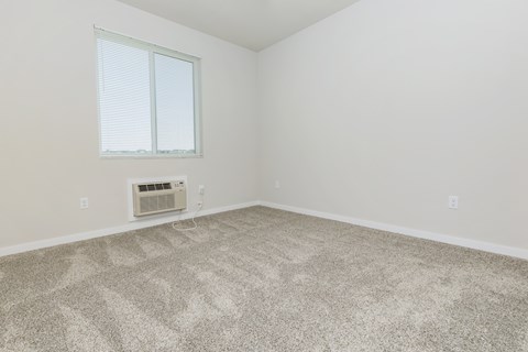 A room with a carpeted floor and a window with blinds.