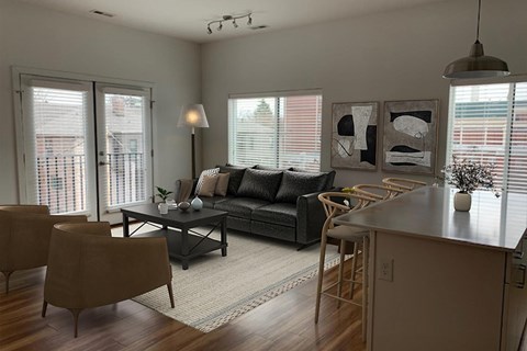 A modern living room with a black couch, a wooden table, and a large window.