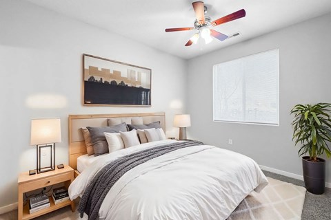 A bedroom with a large bed, a ceiling fan, and a potted plant.